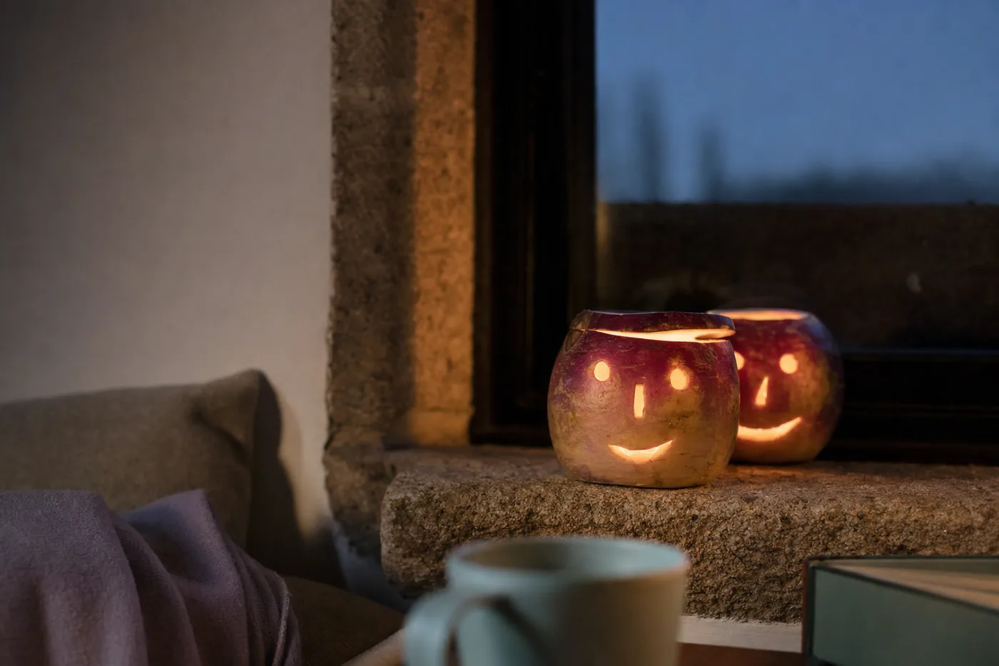 Two carved turnip lanterns glowing on a stone windowsill in the evening